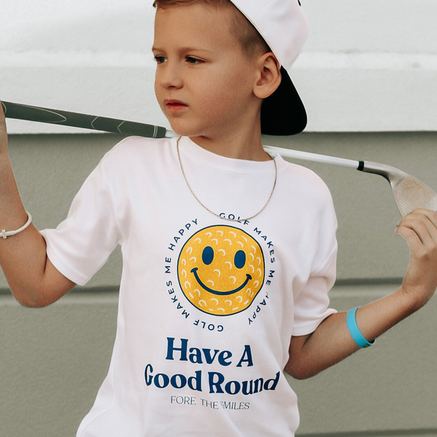 Child wearing a white t-shirt with a smiley face and text, holding a golf club.