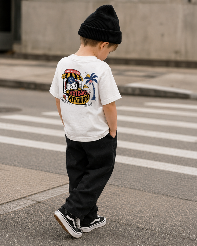 A child wearing a white graphic t-shirt, black beanie, and black pants walking across a street crosswalk.