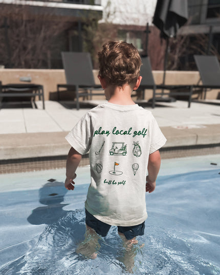 Child standing in a pool wearing a t-shirt with text and graphics.