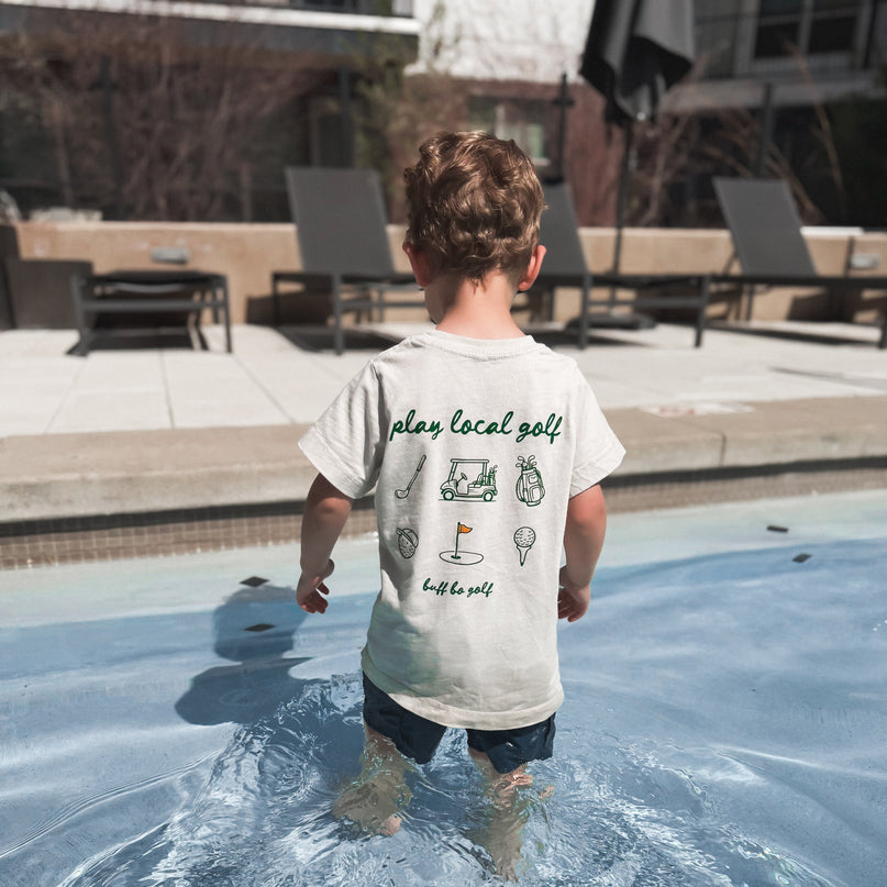 Child standing in a pool wearing a t-shirt with text and graphics.