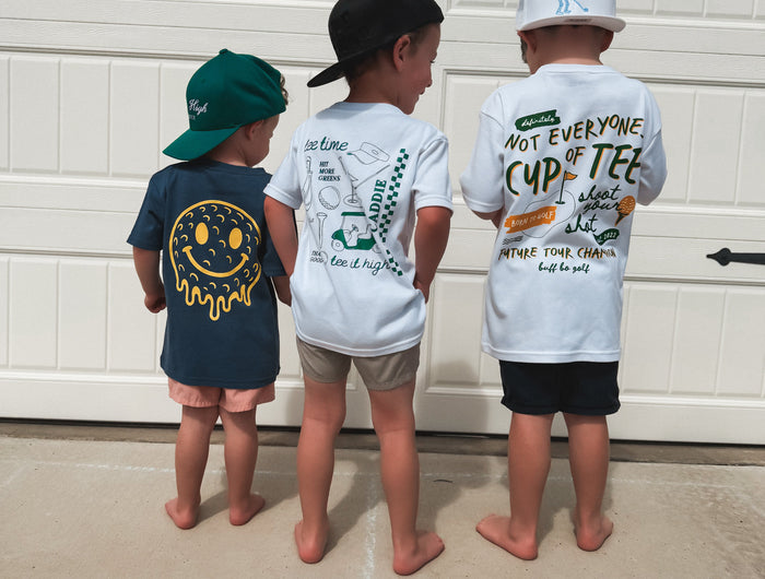 Three children standing in front of a garage door wearing t-shirts with various designs.