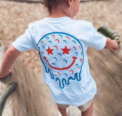 Child wearing a white t-shirt with a colorful smiley face design on a playground.