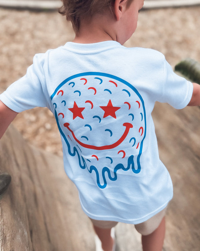 Child wearing a white t-shirt with a colorful smiley face design on a playground.