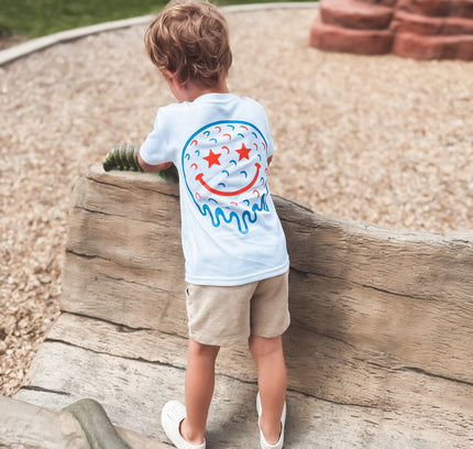 Child wearing a white t-shirt with a colorful design, standing on a log at a playground.