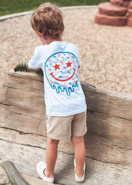 Child wearing a white t-shirt with a colorful design, standing on a log at a playground.