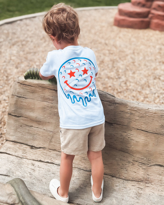 Child wearing a white t-shirt with a colorful design, standing on a log at a playground.