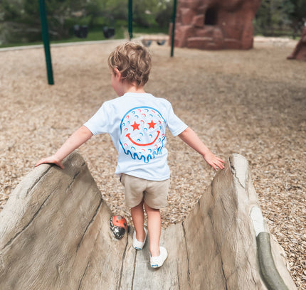 Child climbing on playground equipment wearing a white t-shirt with a colorful design.