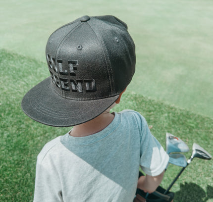 Child wearing a cap with 'Golf Legend' text on a golf course
