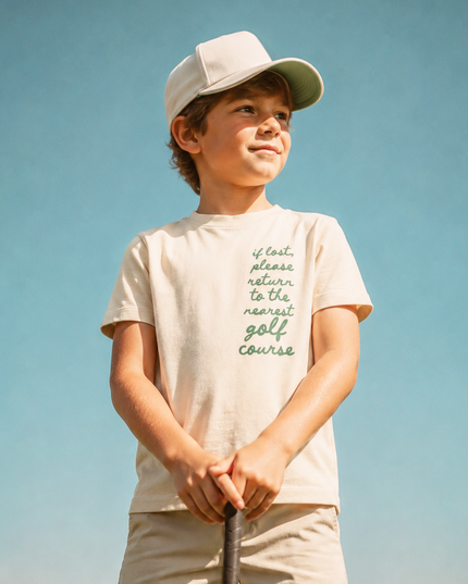 Young boy holding a golf club on a golf course with a clear blue sky.