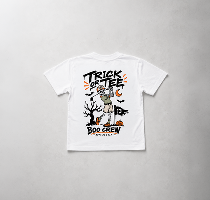 A white short-sleeve t-shirt with a Halloween-themed graphic print on the front, featuring a skeleton in a beige costume, a spooky tree, pumpkins, bats, and the text 'Trick or TEE BOO CREW'. The shirt is laid flat on a textured light gray background.