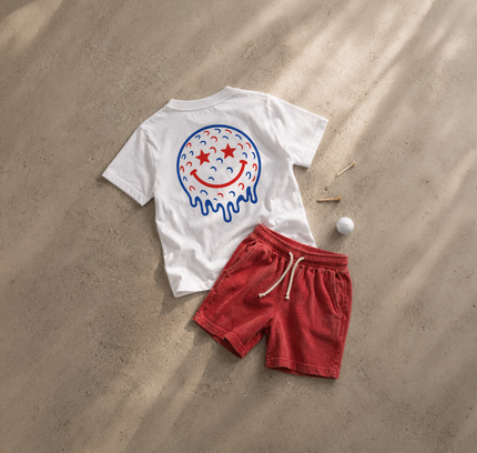 White t-shirt with a colorful smiley face design and red shorts on sand