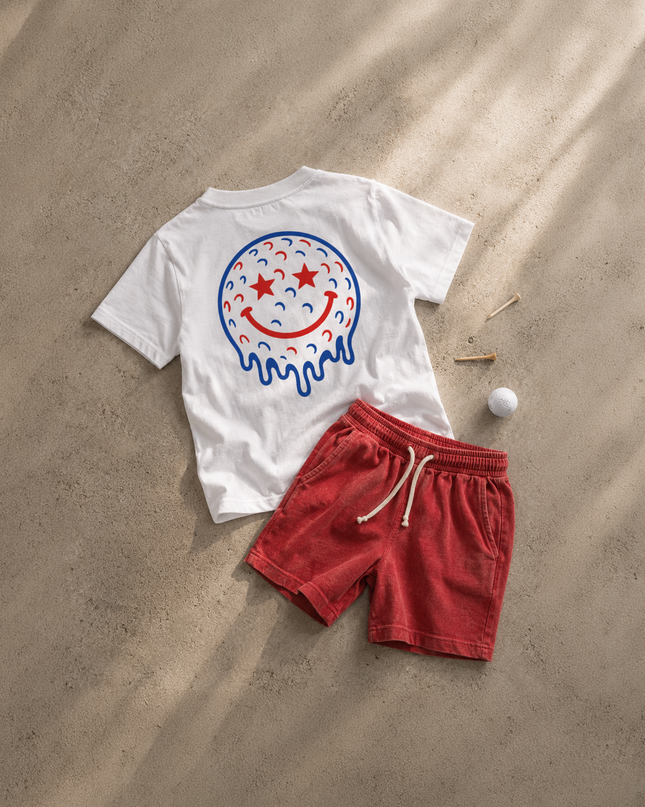 White t-shirt with a colorful smiley face design and red shorts on sand