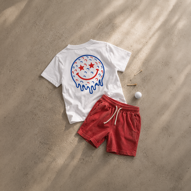 White t-shirt with a colorful smiley face design and red shorts on sand