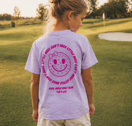 Girl wearing a purple t-shirt with pink graphics and text on a golf course