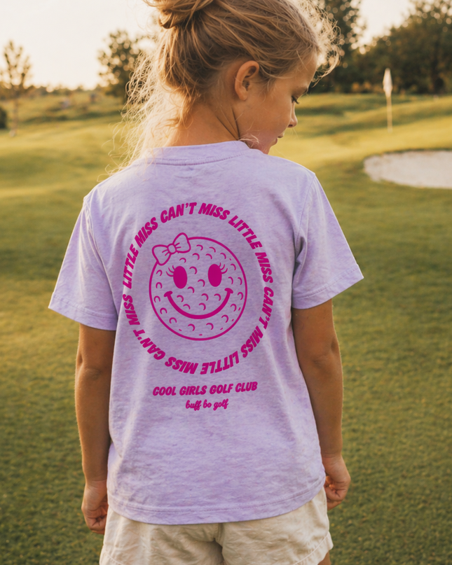 Girl wearing a purple t-shirt with pink graphics and text on a golf course