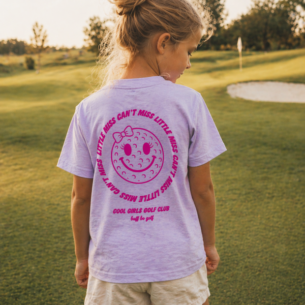 Girl wearing a purple t-shirt with pink graphics and text on a golf course