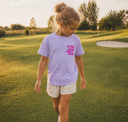 Young girl walking on a golf course wearing a purple t-shirt with text