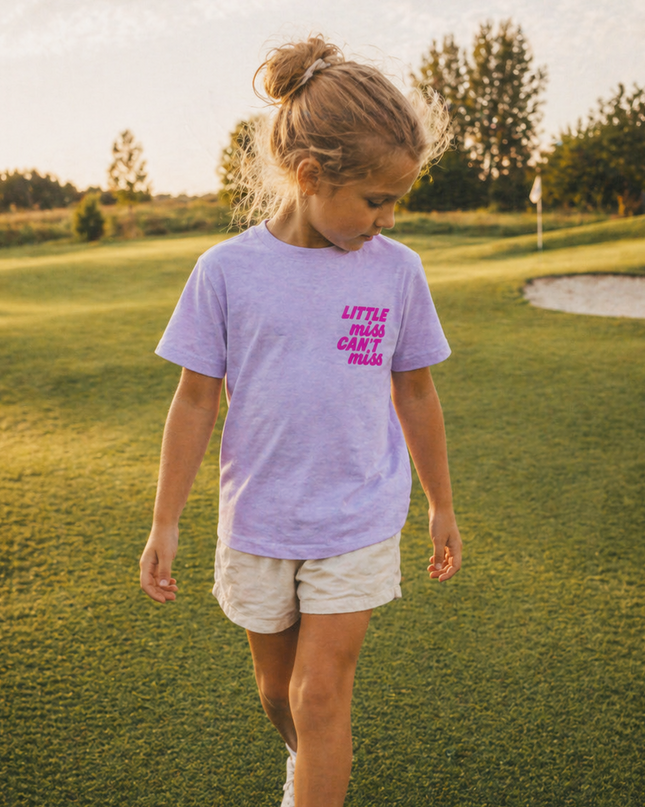 Young girl walking on a golf course wearing a purple t-shirt with text