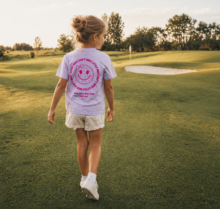 Young girl walking on a golf course with a t-shirt featuring a smiley face design.
