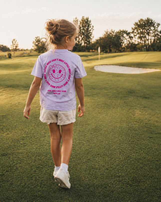 Young girl walking on a golf course with a t-shirt featuring a smiley face design.