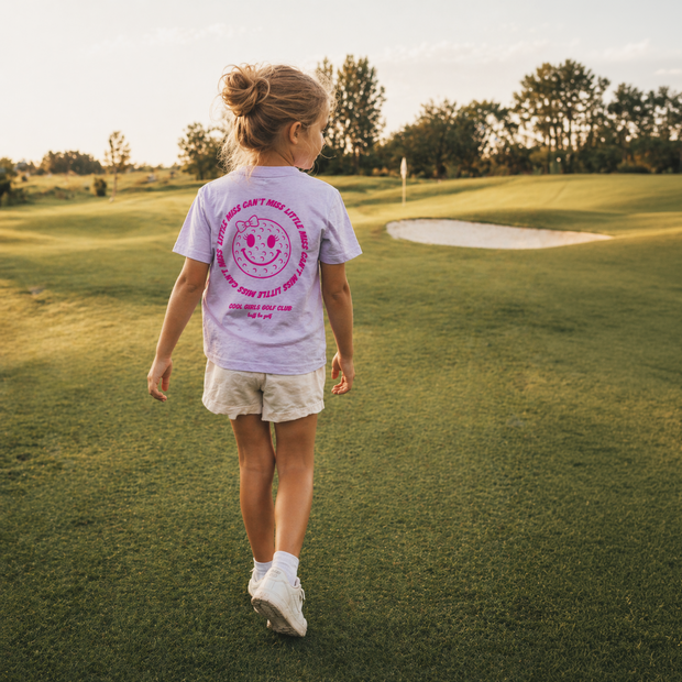 Young girl walking on a golf course with a t-shirt featuring a smiley face design.