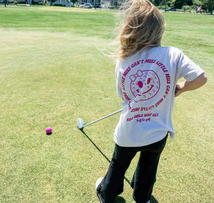 Person on a golf course wearing a white t-shirt with text and graphics.