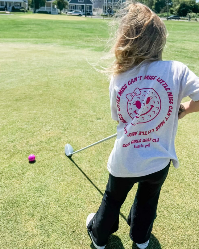 Person on a golf course wearing a white t-shirt with text and graphics.