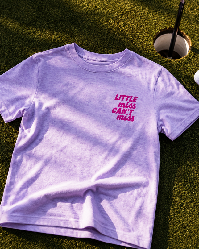 Purple t-shirt with 'Little Miss Can't Miss' text on grass with golf ball and flag