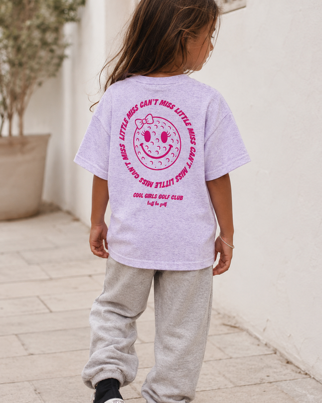 Child wearing a light purple t-shirt with pink text and graphics outdoors.