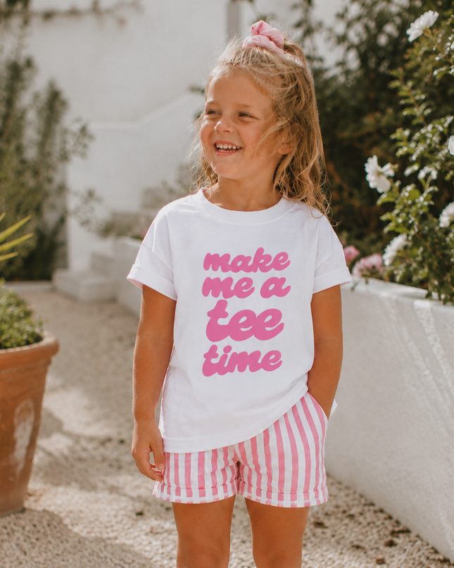 Young girl wearing a white t-shirt with pink text and striped shorts, standing outdoors.