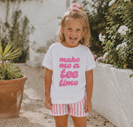 Young girl wearing a white t-shirt with pink text and red and white checkered shorts outdoors.