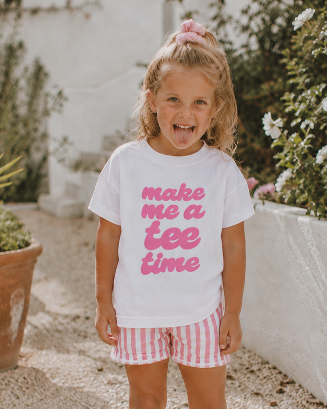 Young girl wearing a white t-shirt with pink text and red and white checkered shorts outdoors.