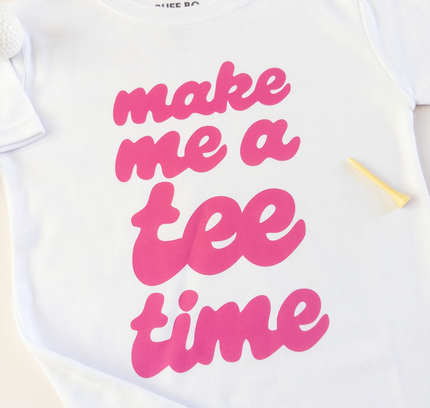 White t-shirt with pink text 'make me a tee time' on a light background