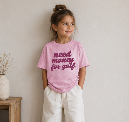 Young girl wearing a pink t-shirt with text, standing against a plain wall.
