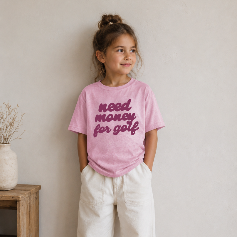 Young girl wearing a pink t-shirt with text, standing against a plain wall.