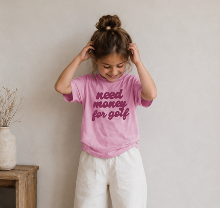 Child wearing a pink t-shirt with text, standing indoors against a plain wall.