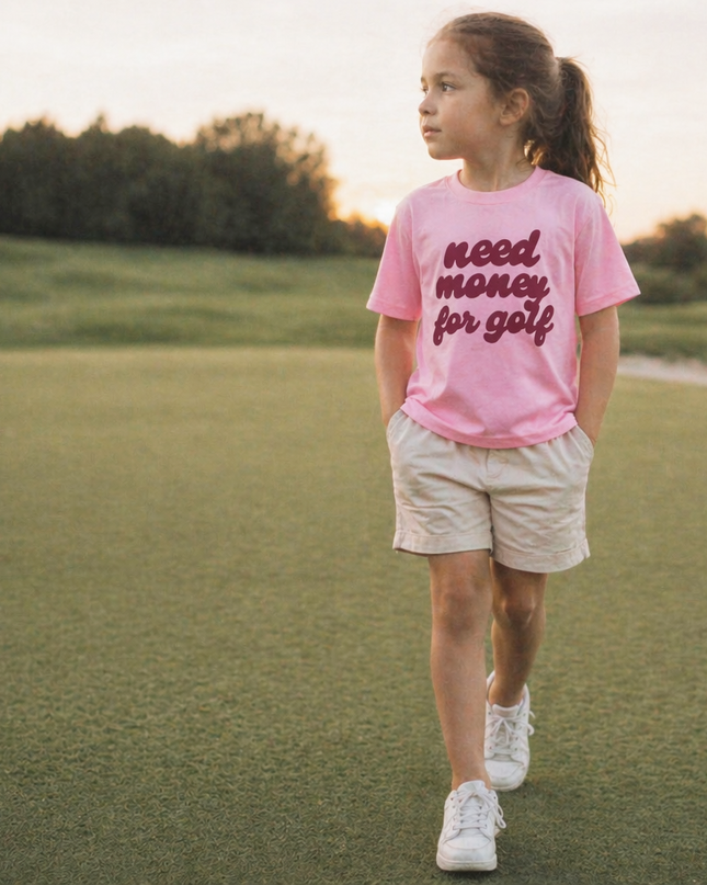 Young girl in a pink shirt with text standing on a grassy field.