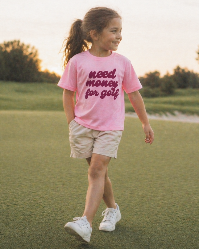 Child wearing a pink t-shirt with text, walking on a grassy field.