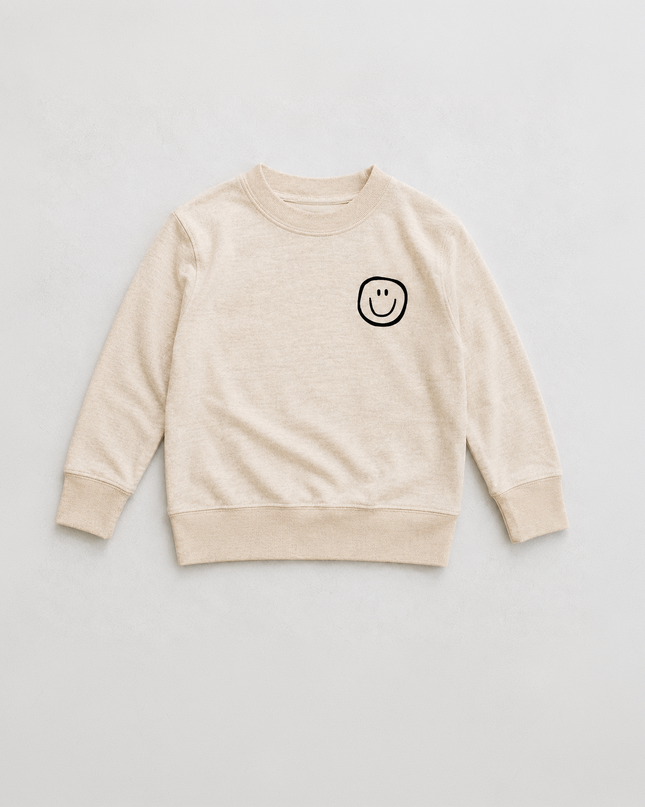 A light beige crewneck sweatshirt with a small black smiley face graphic on the left chest, laid flat against a light gray background.