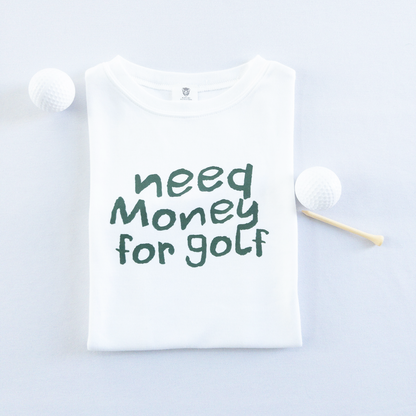 White kids golf t-shirt with playful dark green text reading 'Need Money for Golf,' displayed flat with golf balls and a wooden tee, fun and casual golf apparel for young golfers.