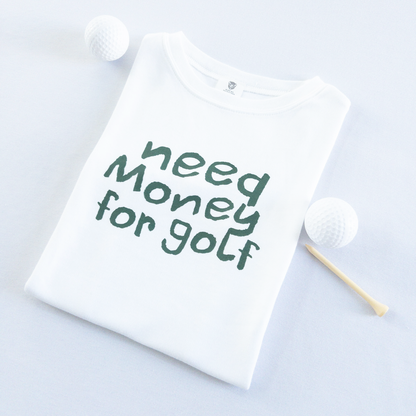 White kids golf t-shirt with playful dark green text reading 'Need Money for Golf,' displayed flat with golf balls and a wooden tee, fun and casual golf apparel for young golfers.