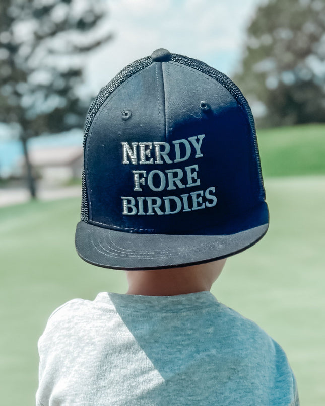 Child on a golf course wearing a cap with 'Nerdy Fore Birdies' text