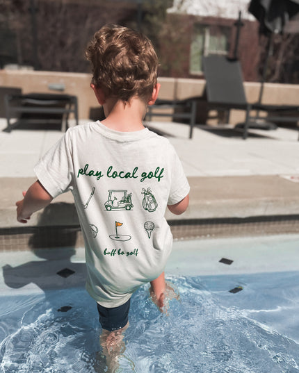 Child walking into a pool wearing a t-shirt with text and graphics.