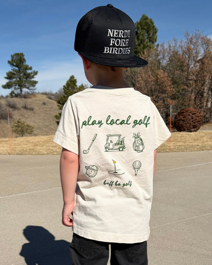 Child wearing a cap and t-shirt with graphics and text, standing on a paved road with a clear sky.