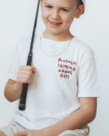 Child wearing a white t-shirt with text and holding a golf club on a light background