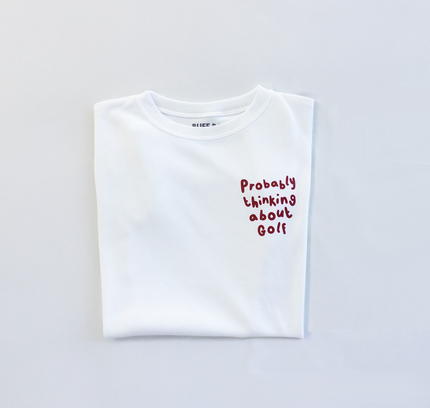 White t-shirt with text 'Probably thinking about golf' on a light gray background