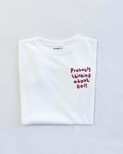 White t-shirt with text 'Probably thinking about golf' on a light gray background