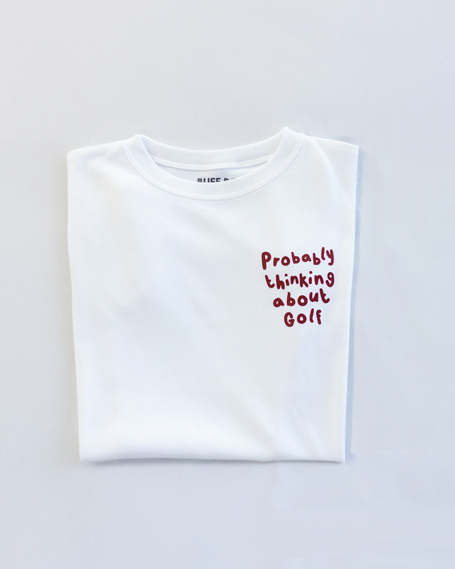 White t-shirt with text 'Probably thinking about golf' on a light gray background
