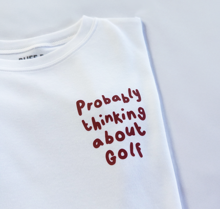 White t-shirt with red text 'Probably thinking about Golf' on a light gray background