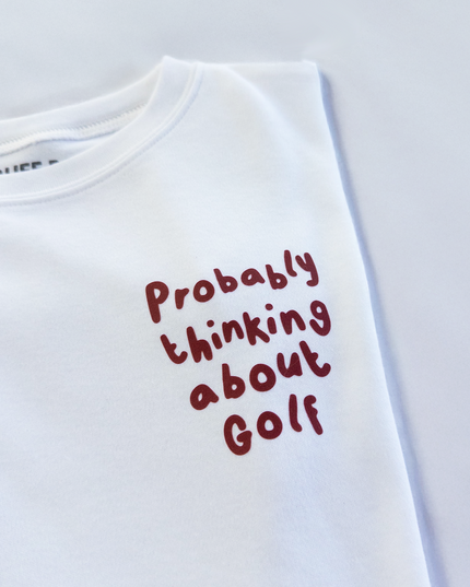 White t-shirt with red text 'Probably thinking about Golf' on a light gray background